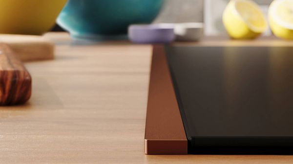 Detailed view of a NEFF induction hob with Flex Design side trim in Brushed Bronze, integrated into a light wooden countertop.