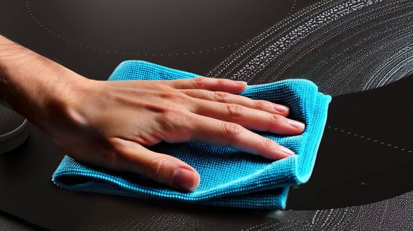 Hand with a cloth cleaning matt black hob