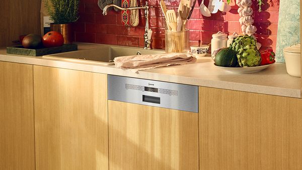 Una cucina dotata di lavastoviglie in acciaio inossidabile, mobili in legno, lavandino e verdure fresche sul piano di lavoro.