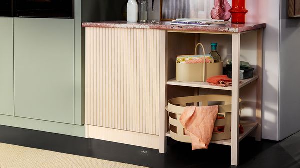 Стилен кухненски ъгъл с текстуриран бежов шкаф, мраморен плот и организирани кошници с ярки тъкани и кухненски принадлежности.