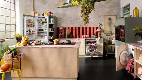 Een keuken met een groot eiland vol verse producten, een open koelkast en keurig georganiseerde keukenapparatuur.   