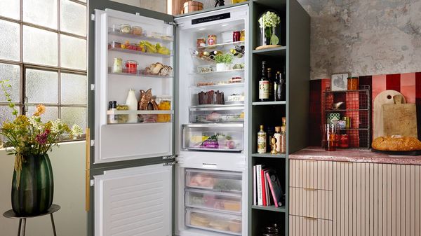 Woman holding a tray in front of an open fridge, while a man looks on, with food items displayed. 
