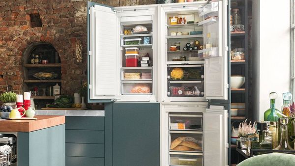 A man standing in front of an open refrigerator, inspecting food options.