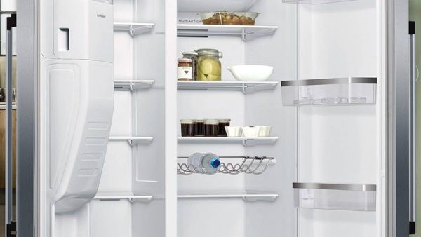 A man standing in front of an open refrigerator, inspecting food options.