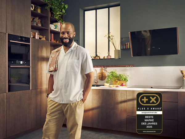 Mann steht in moderner NEFF K&uuml;che mit Einbauger&auml;ten; Plus X Award Siegel &bdquo;Beste Marke des Jahres 2025&ldquo; sichtbar &ndash; ausgezeichnetes Design und Flex Design im Fokus.