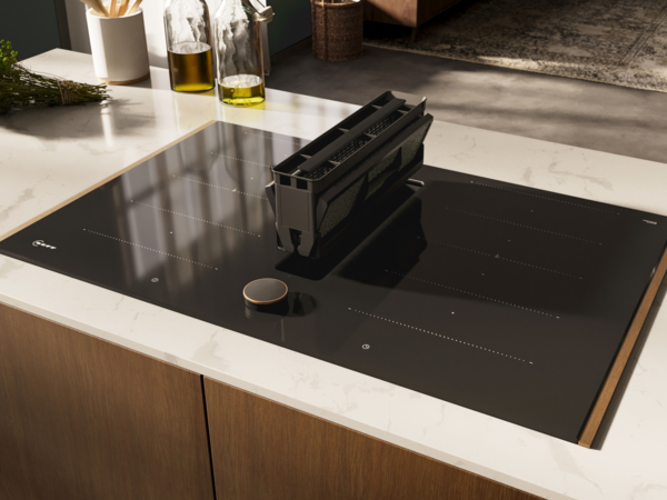Integrierter Kochfeldabzug mit herausgenommenem Filtereinsatz auf schwarzem Induktionskochfeld.