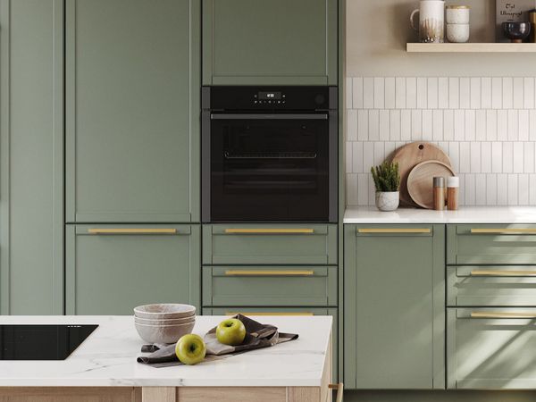 Просторна светла кухня с дървени и зелени шкафове и фурна Neff