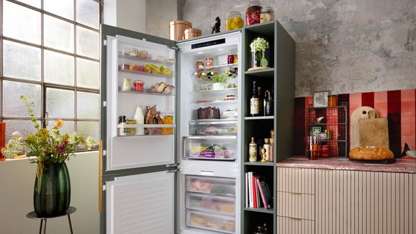 A man standing in front of an open refrigerator, inspecting food options.