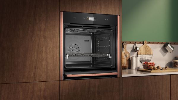 Forno da incasso NEFF integrato in una cucina con mobili in legno scuro e piano di lavoro con utensili