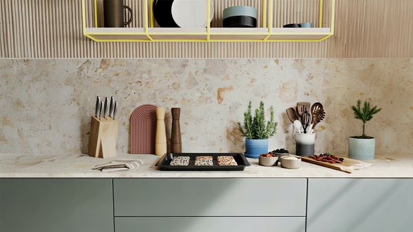 A modern kitchen counter with various cooking utensils, plants, and a tray of food.