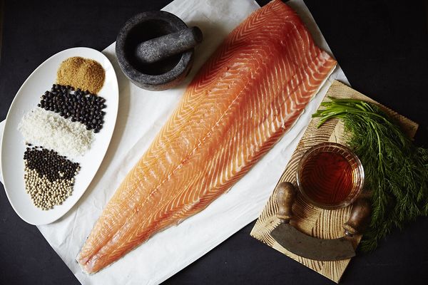 Filetto di salmone fresco su carta da forno con spezie, mortaio e ciotola di salsa su sfondo scuro