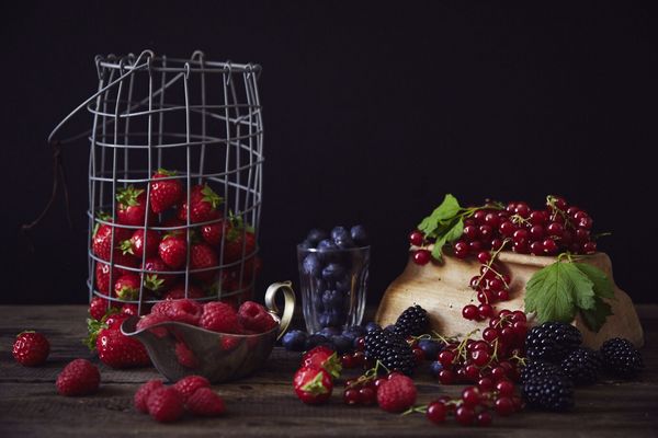 Composizione di frutti di bosco con fragole, lamponi, mirtilli, more e ribes su tavolo in legno con sfondo scuro