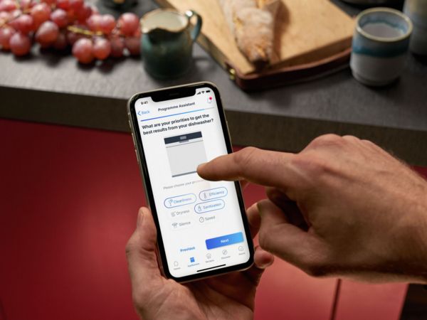 Ein Mann steht vor dem Backofen und sieht auf sein Smartphone.