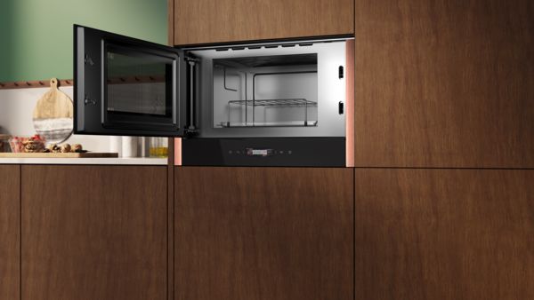 Microonde da incasso NEFF con porta aperta e interno illuminato, integrata in una cucina con mobili effetto legno