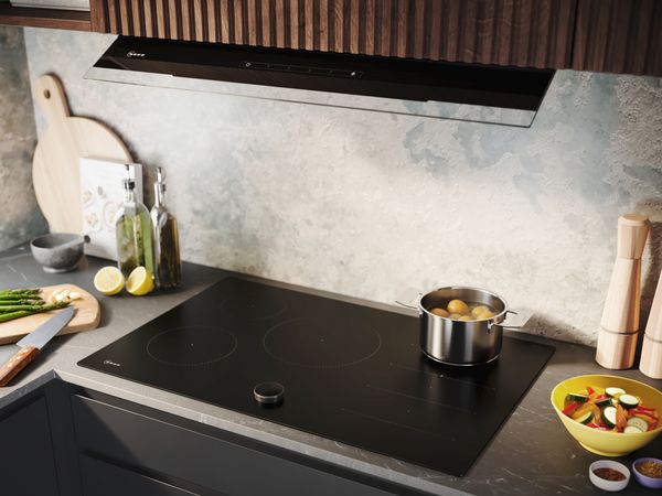 Un piano cottura a induzione nero ed elegante, con verdure fresche, un vasetto di limoni e vari utensili da cucina sparsi intorno, in una cucina arredata in stile moderno.