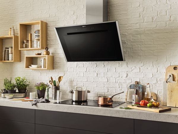 Egy modern konyha jellemzője egy fekete elszívó, rozsdamentes acél edények, fűszernövények és színes paradicsomok egy fa vágódeszkán. Friss és stílusos