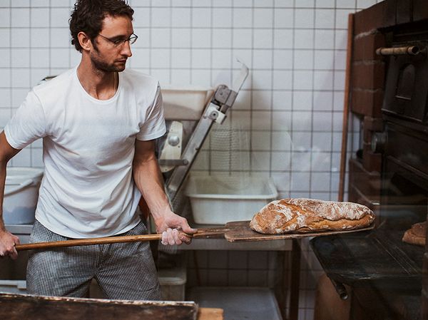 Man putting loaf of bread in to a bread oven