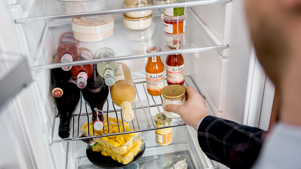 Detailansicht eines NEFF Kühlschranks mit Bottle Flex Shelf: Zwei Glasflaschen liegen sicher in einem flexiblen Flaschenhalter auf einer Glasablage.