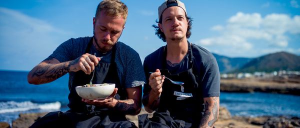 Men eating food out of a bowl next to the sea