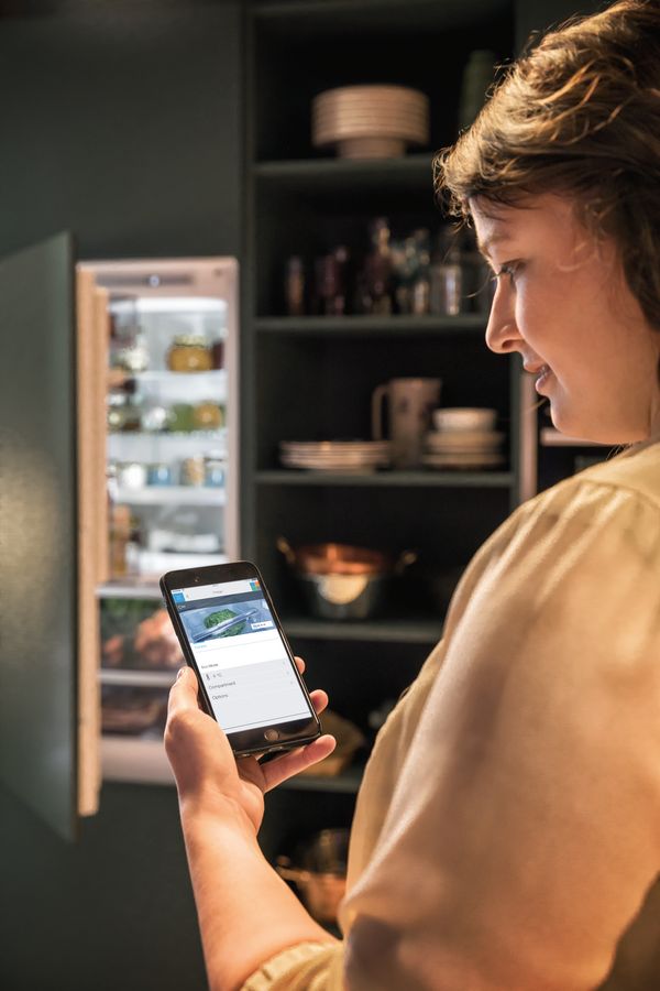 Giovane donna che controlla il suo frigorifero dallo smartphone grazie a una app 