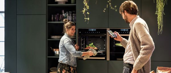 Девушка и молодой человек готовят ужин с духовым шкафом NEFF и приложением Home Connect