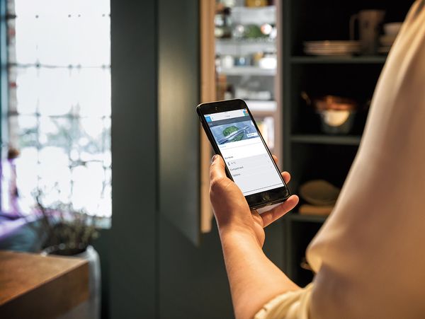 Person using Home Connect app on mobile phone in kitchen with NEFF built-in appliances