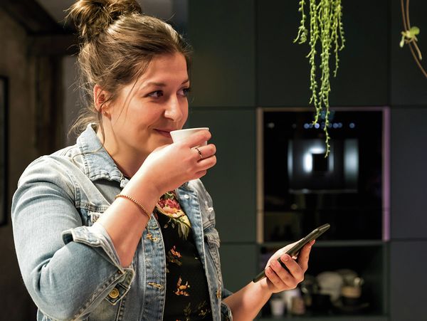 Woman smelling freshly brewed coffee from NEFF built-in bean-to-cup coffee machine