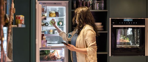 Giovane donna che prende una bottiglia da uno scaffale del frigorifero a casa