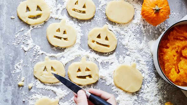 Person using knife to cut out eyes and mouth holes in pumpkin shaped dough