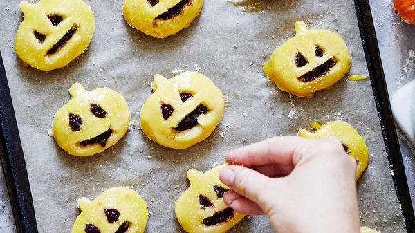Person sprinkling sugar on top of pumpkin pasties in baking tray before cooking 