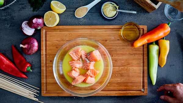 Σολομός μαριναρισμένος με κίτρινη σάλτσα, συνοδευόμενος από φρέσκα λαχανικά και φέτες λεμονιού σε ξύλινο ταμπλό.