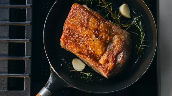 A perfectly roasted beef joint with a crispy exterior, garlic cloves, and fresh herbs, sizzling in a cast iron skillet.