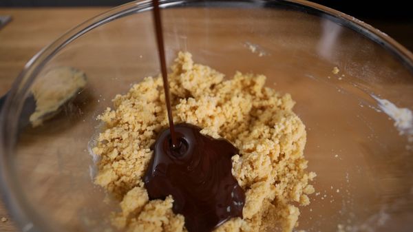 Melted dark chocolate being poured over ingredients in bowl