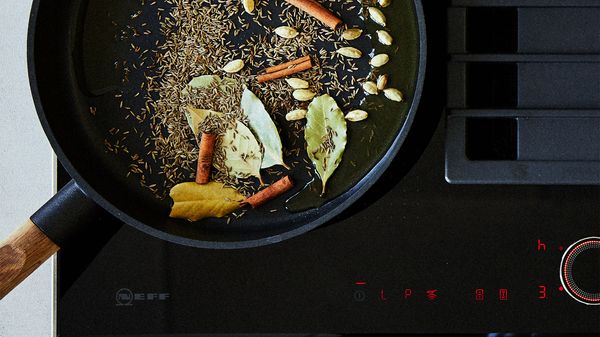 Pan frying ghee, cashewnuts, bay leaves and other ingredients on an induction hob