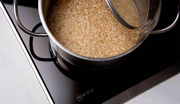 Brown rice and water in a steel saucepan, placed on a NEFF induction hob