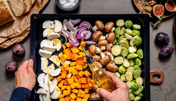 Drizzling olive oil over a tray of vegetables